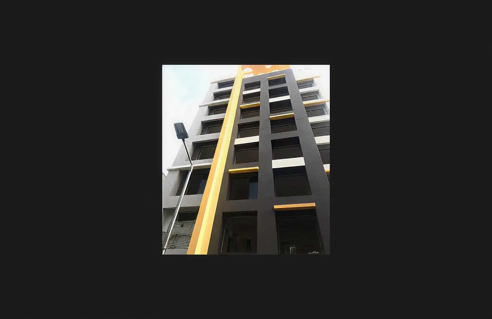 A modern mid-rise residential building captured from a low-angle view, showcasing a newly completed façade with bold grey and yellow elevation elements and clean rectangular window openings. The structure reflects contemporary exterior finishing and precise façade detailing, representing high-quality residential construction.