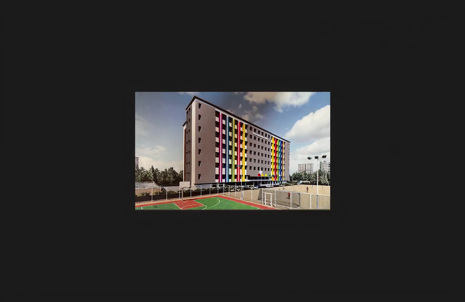 A newly developed multi-storey institutional and residential building featuring a modern elevation with colourful vertical panels and uniform window alignment. The property includes a landscaped outdoor sports court in the foreground, demonstrating large-scale construction capability and precise architectural planning.
