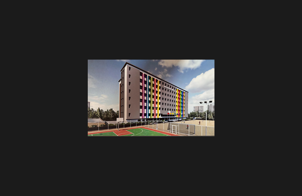 A multi-storey institutional building featuring vertical rainbow-colored façade elements and a modern grey exterior, with outdoor sports facilities including a basketball court and tennis court in the foreground under a partly cloudy sky.