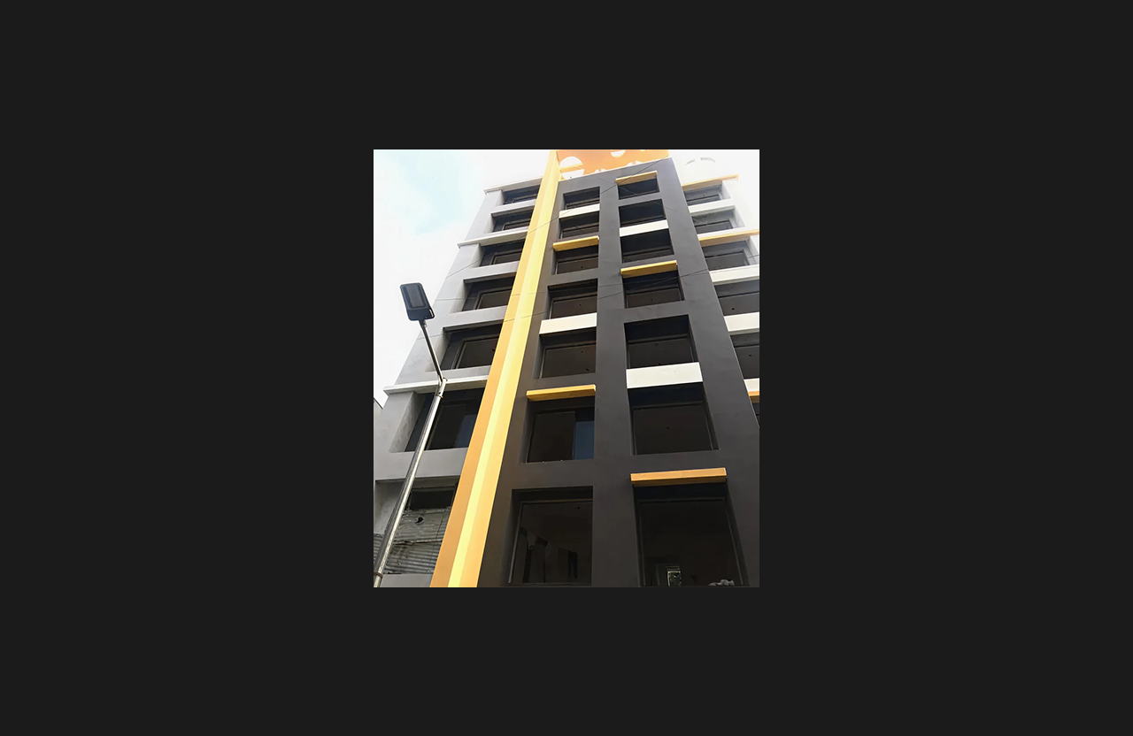 A close-up low-angle view of a modern multi-storey building façade with bold black and yellow architectural elements and large window openings, showcasing contemporary exterior styling under a clear sky.