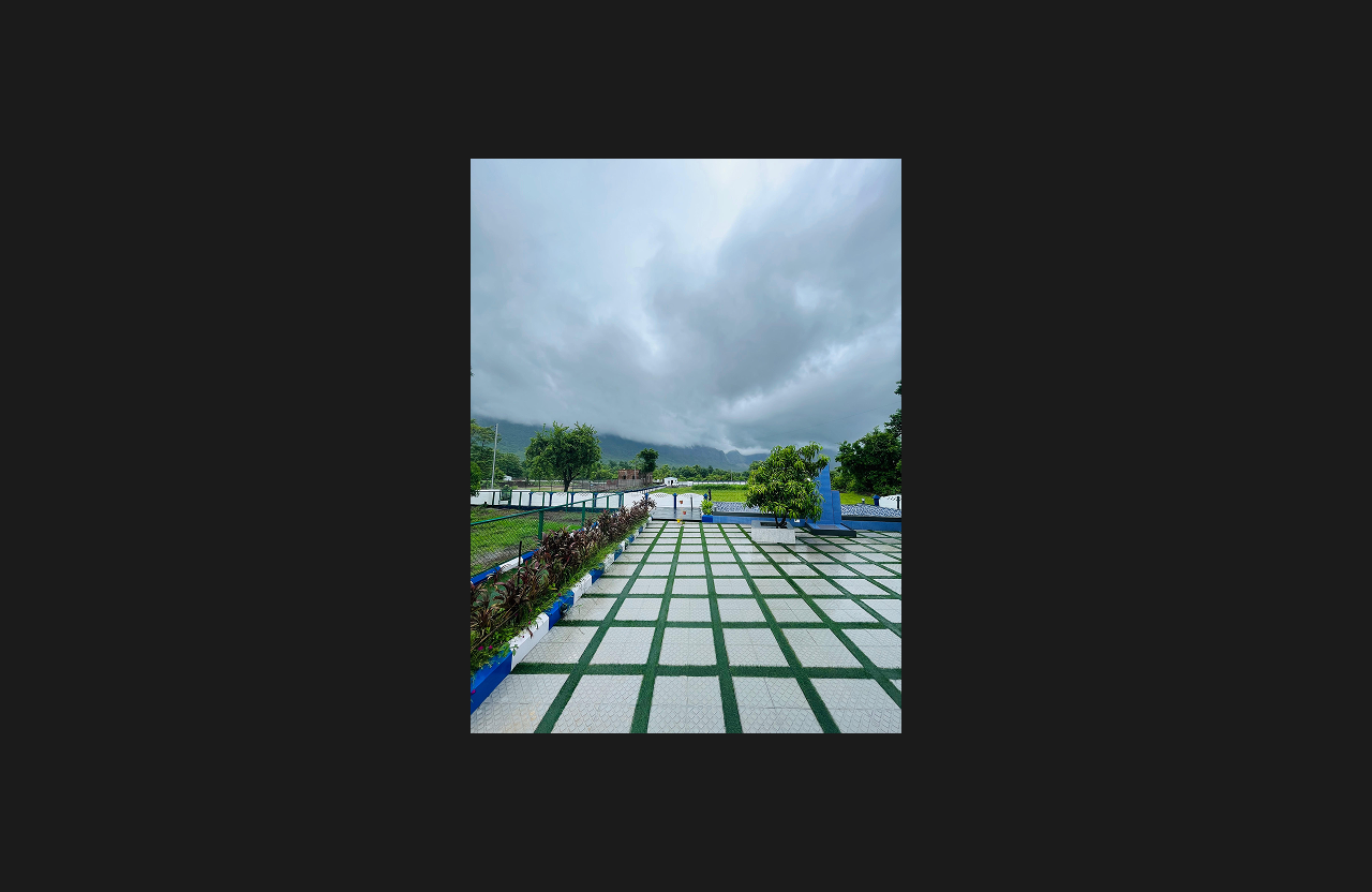 A beautifully paved courtyard surrounded by planters and fencing, opening to panoramic views of lush green fields and mist-covered mountains under dramatic cloudy skies.