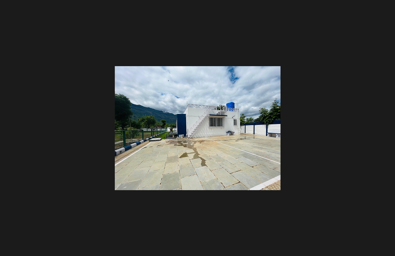 A modern white farmhouse with a terrace staircase and open patio space, situated against a scenic mountain backdrop surrounded by greenery and open land.