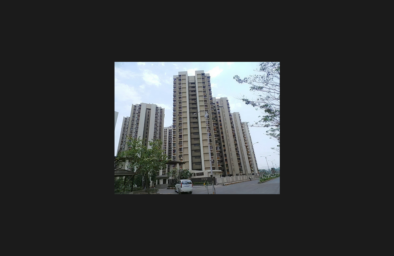Wide street-level view of a cluster of premium high-rise residential buildings with symmetrical vertical elevation design, surrounded by greenery and open driveway space under a partly cloudy sky.